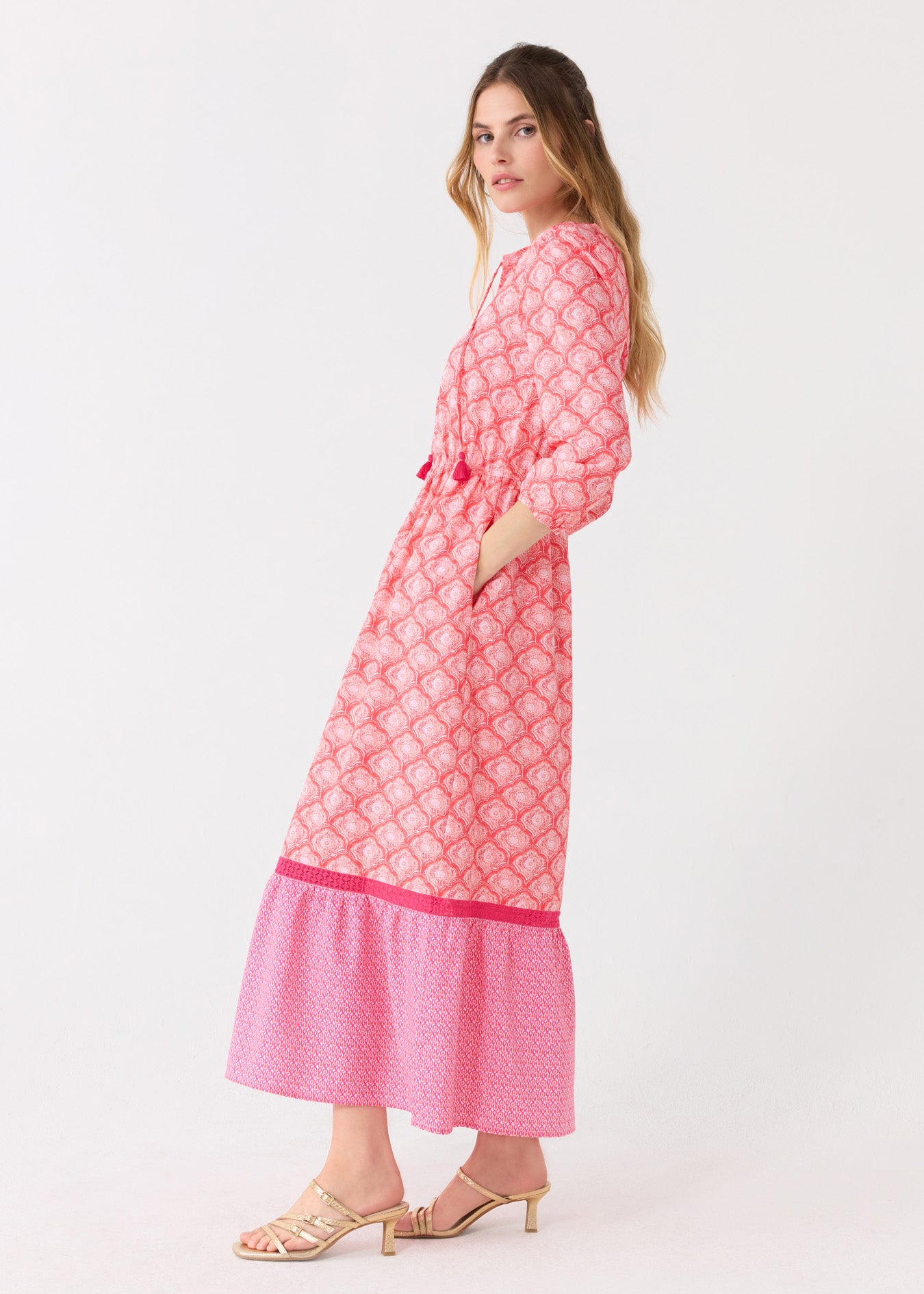 The side of a blonde woman wearing the Cabana Life sun protective Amelia Island Relaxed Maxi Dress and gold sandals with a hand in her pocket.