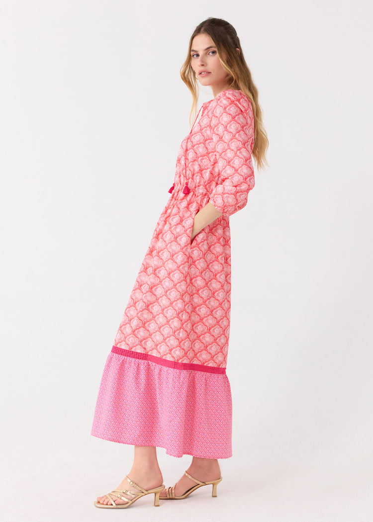 The side of a blonde woman wearing the Cabana Life sun protective Amelia Island Relaxed Maxi Dress and gold sandals with a hand in her pocket.