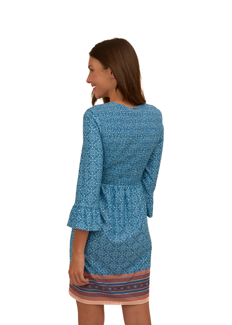 The back of a brunette woman wearing Cabana Life's sun protective Camden Leaf Smocked Babydoll Dress on a white background.