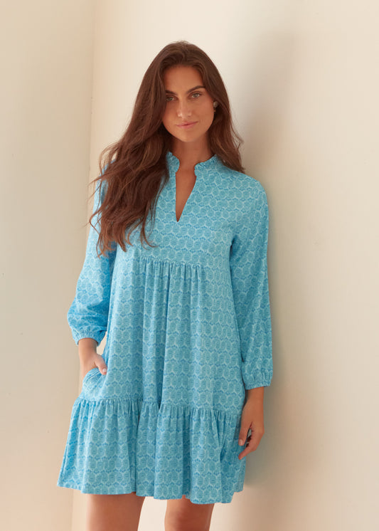 A brunette woman wearing the Cabana Life sun protective Rosebay Relaxed Dress against a wall with a hand in her pocket.