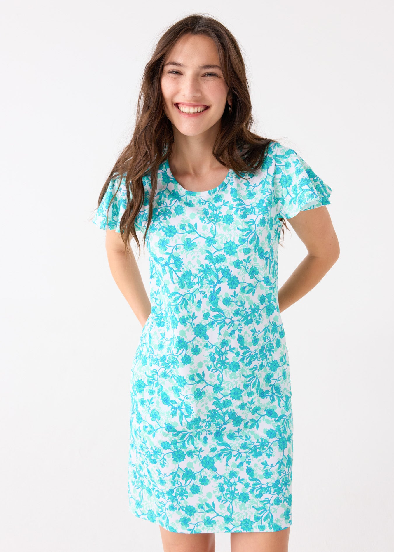 A brunette woman with hands behind her back wearing the Cabana Life sun protective Rosebay Ruffle Short Sleeve Dress.