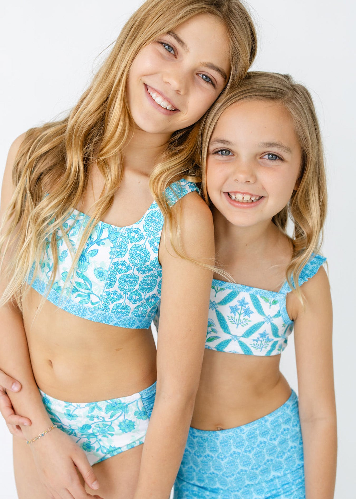 Blonde girls wear bikinis from Cabana Life's sun safe Girls Rosebay 3-Piece Short Sleeve Rashguard Set and Girls Rosebay 3-Piece Long Sleeve Rashguard Set.