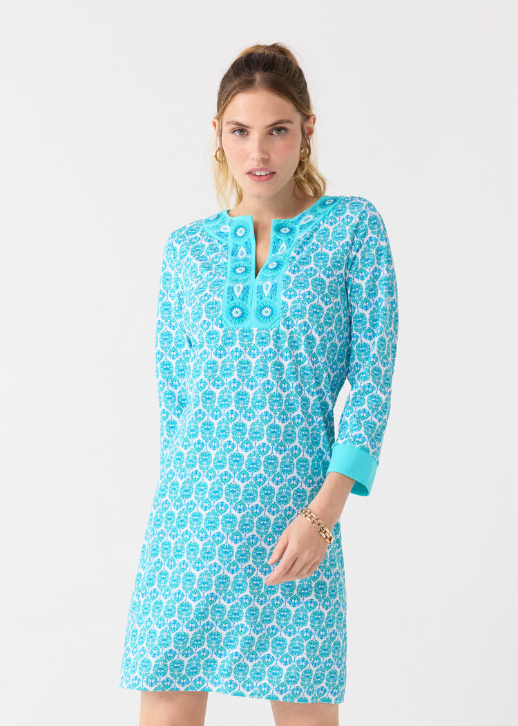 A woman with her hair up in a ponytail wearing the Cabana Life sun protective Rosebay Embroidered Tunic Dress with gold jewelry.