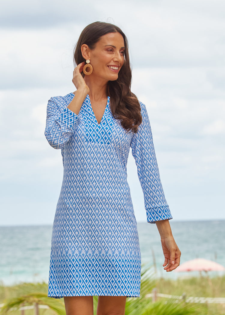 Brunette woman wearing our UPF 50+ Seaside Tunic Dress standing on a beach with her hand behind her ear.