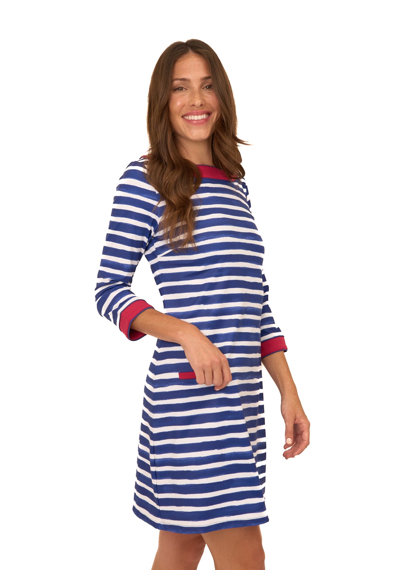 A brunette woman wearing Cabana Life's sun protective Watercolor Stripe Cabana Shift Dress with her hand in front of her pocket on a white background.