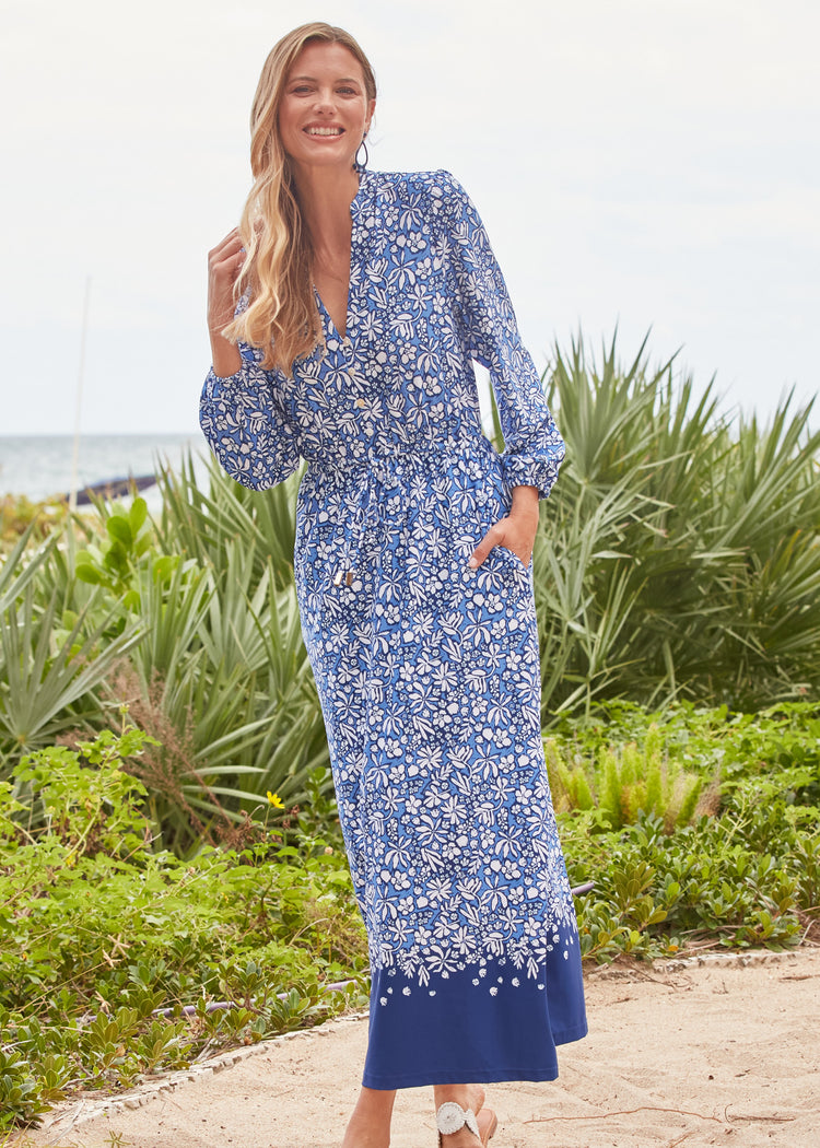 Woman wearing a blue floral dress standing outdoors with greenery in the background