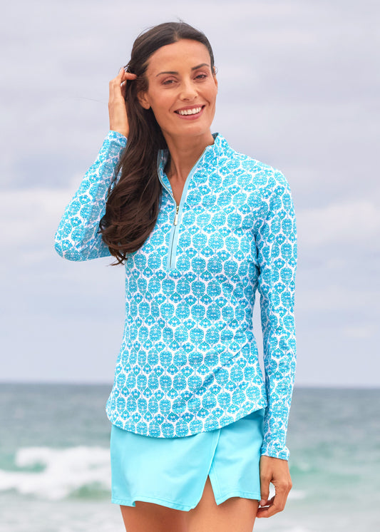 A brunette woman wearing the Cabana Life sun protective Rosebay Performance 1/4 Zip Sport Top with mesh underarms, paired with the Aqua Classic Swim Skirt on the beach.
