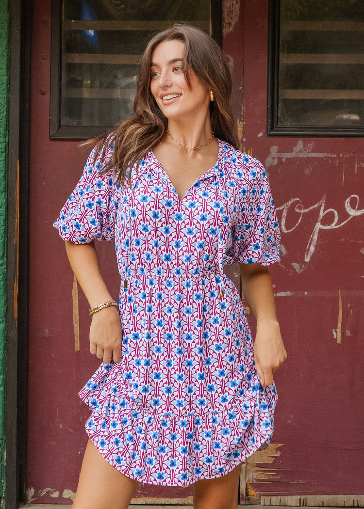 Woman wearing a patterned dress standing in front of a red door.