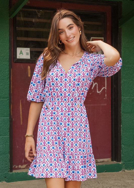 Woman wearing a colorful patterned dress standing in front of a green wall.