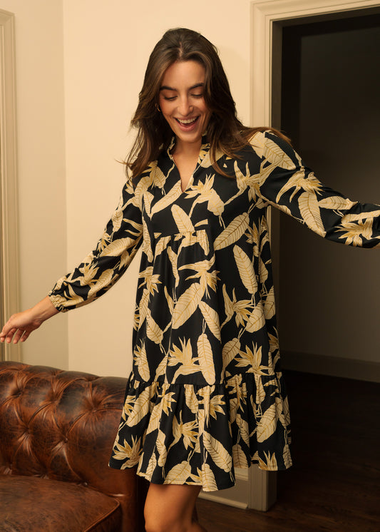 Woman wearing a black dress with gold patterns in a room.