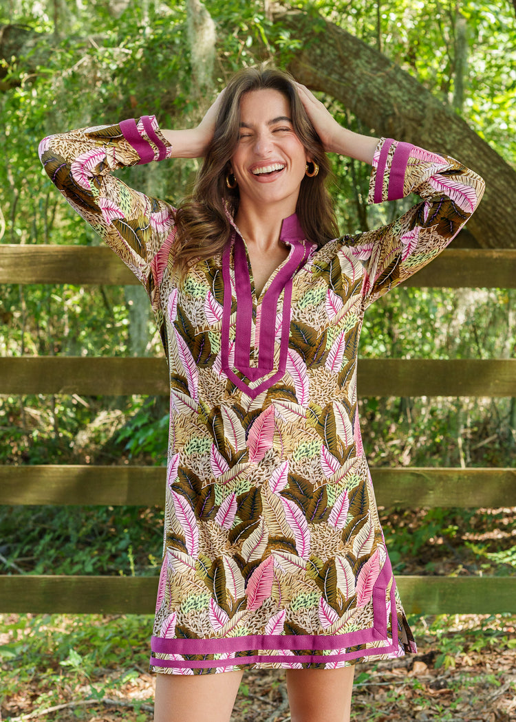Woman wearing a patterned dress with long sleeves, standing outdoors near a wooden fence.