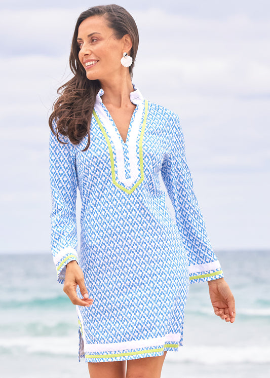 A brunette woman smiling and walking on the beach wearing the Cabana Life sun protective Seaside Pique Tunic Dress.