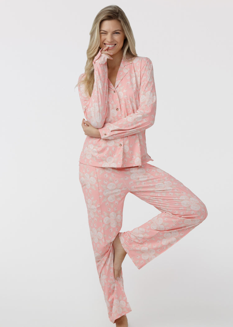 Woman standing, wearing our Coast pink and white shell patterned sleep to street pajama set on a white background.