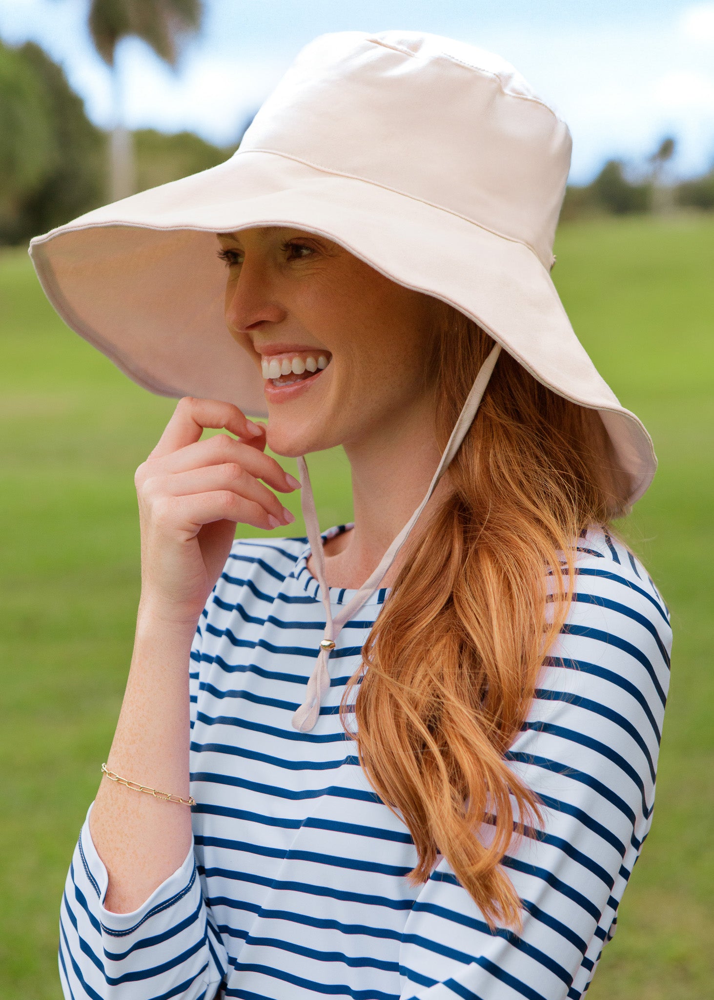 Woman wearing a wide-brimmed beige hat and striped dress outdoors.