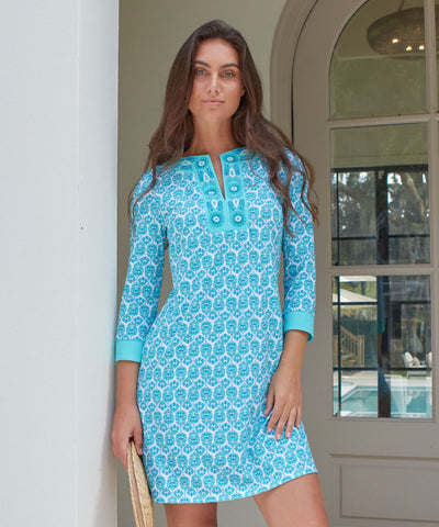 Woman wearing a teal and white printed dress against a beige wall.