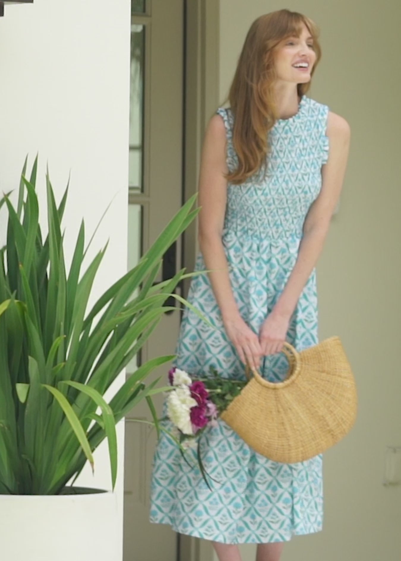 A redheaded woman outside a house wearing the Cabana Life sun protective Rosebay Smocked Maxi Dress.