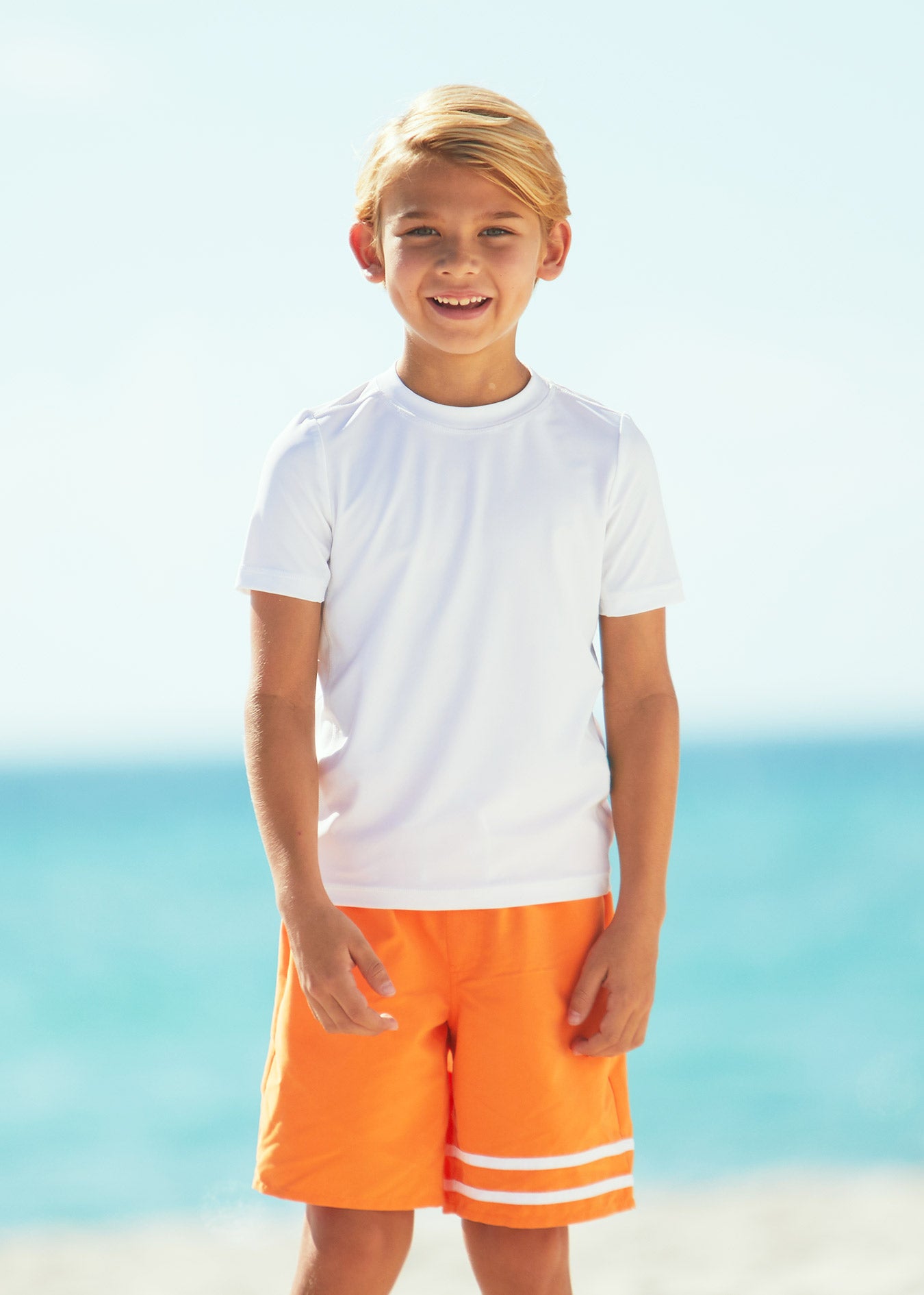 Boy on beach wearing Boys White Short Sleeve Rashguard with Boys Tangerine Swim trunks