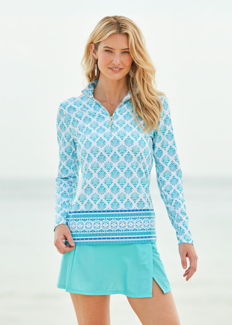 Blonde woman on beach wearing Amalfi Coast Sport Zip Polo with Aqua Classic Swim skirt.