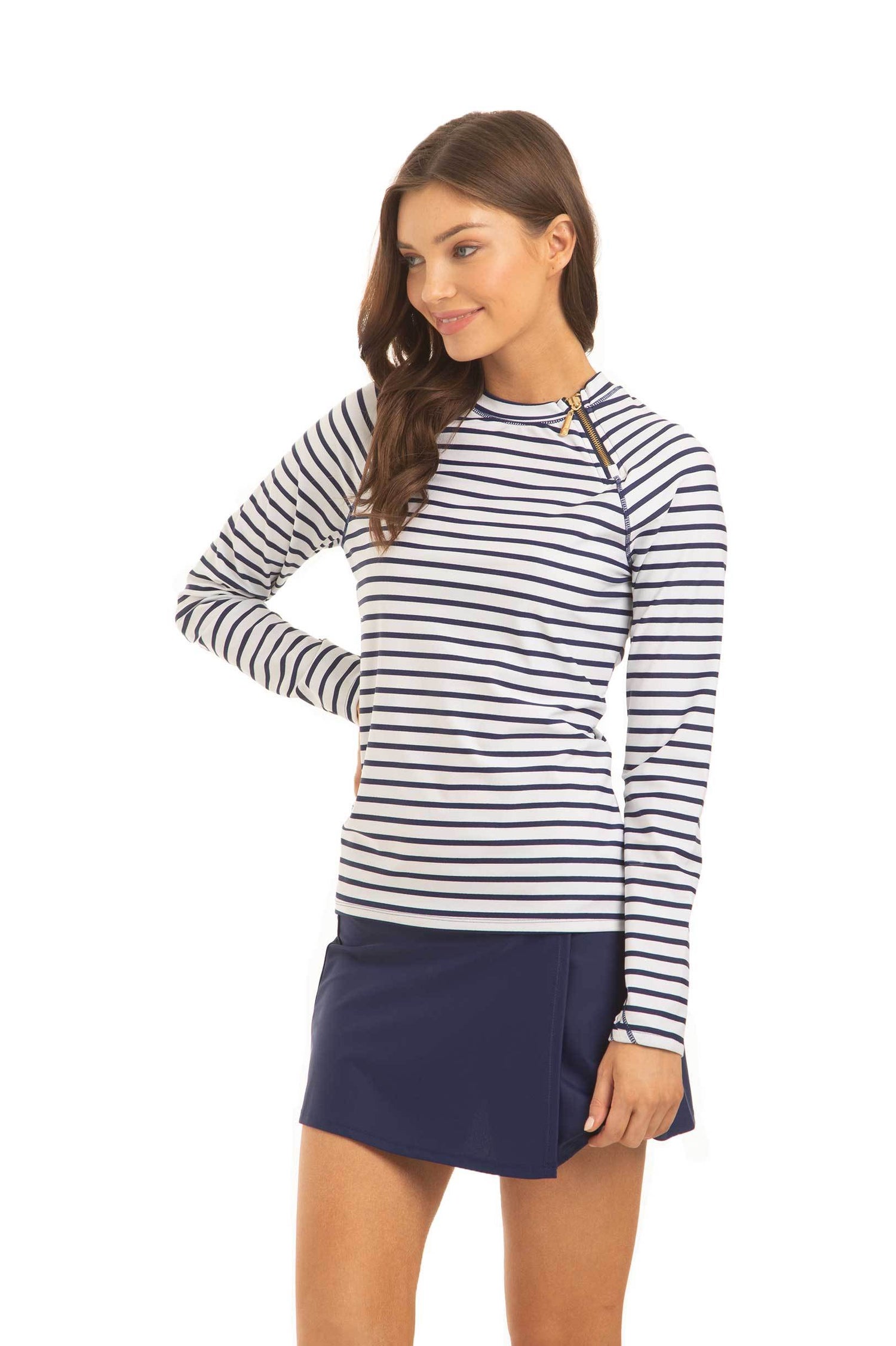A brunette woman with her hand on her  hip facing the side and wearing the Cabana Life sun protective Navy Stripe Zipper Rashguard and Navy Classic Swim Skirt.