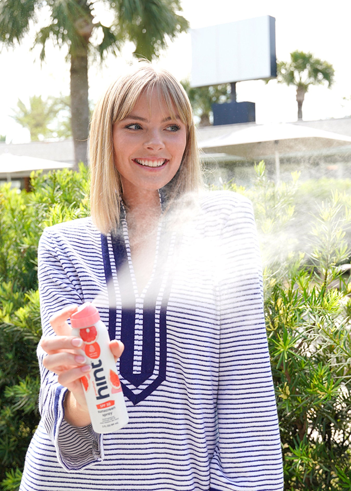 Woman wearing Navy Stripe Terry and spraying Hint sunscreen
