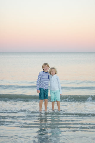 Boy wearing Boy's Navy Stripe Rashguard with Aruba Blues Swim Trunks and boy wearing white rashguard with Boy's Coral Tides Swim Trunks