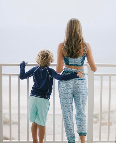 Woman wearing Aruba Blues Bikini Top and Aruba Blues Beach Pants With Tie and boy wearing long sleeve navy rashguard with Coral Tides Swim Trunks