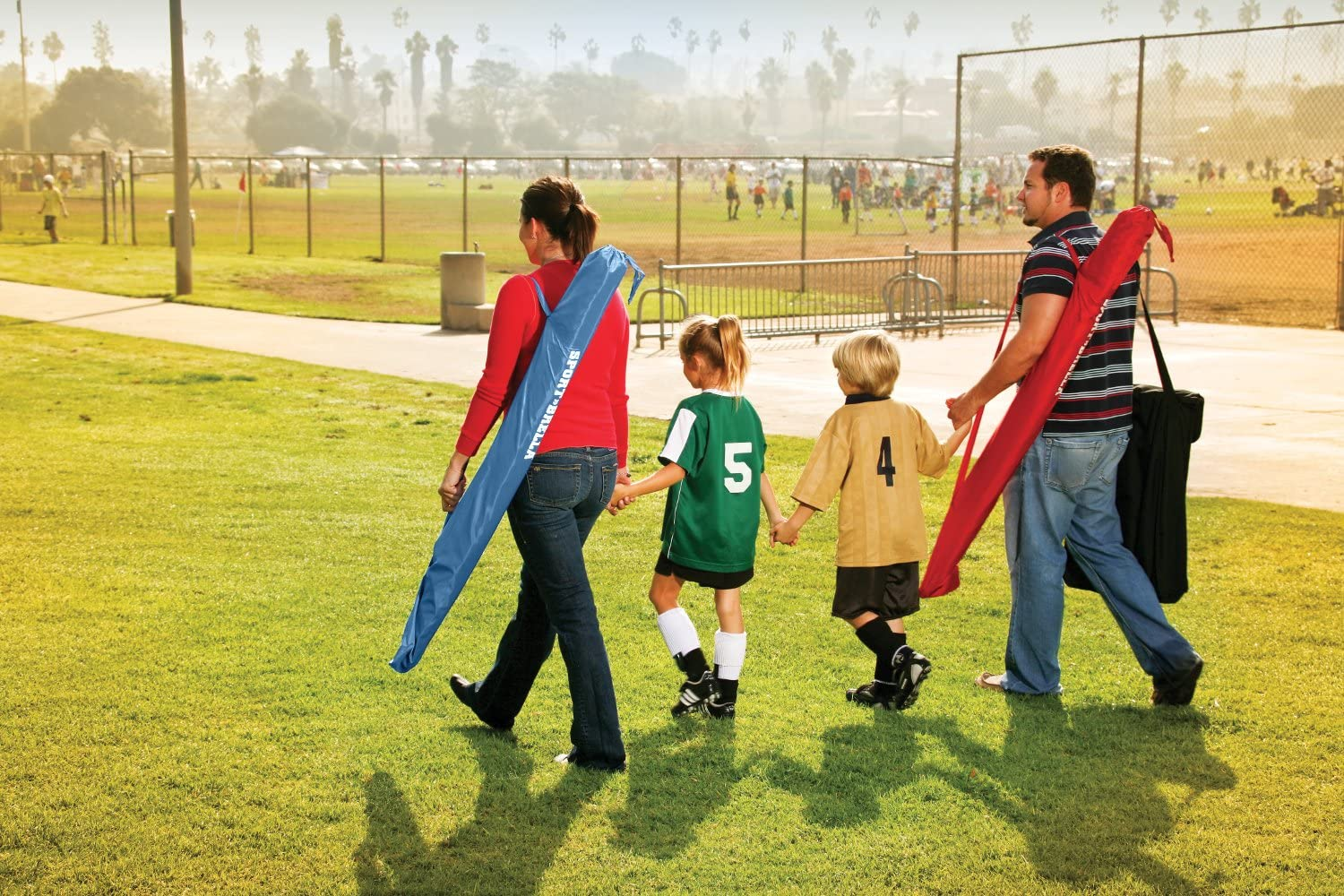 Family walking across grass at soccer game. Man and woman each carrying carrying a Sport-Brella XL over their shoulder